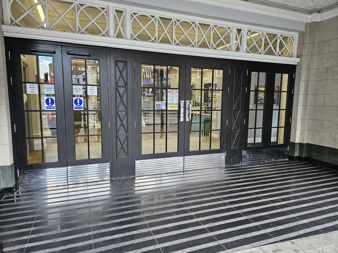 Winding Wheel Theatre entrance doors. A set of dark brown wooden doors with multiple panes of glass in each.